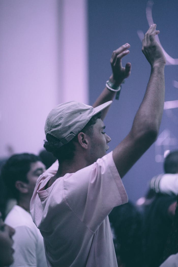 A young adult in a crowd raises arms in celebration or worship, capturing a moment of communal joy.